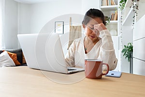 Young Asian woman feeling tired and having headache after working long hours at home office.