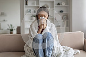 Young asian woman feeling unwell at home, sneezing into tissue