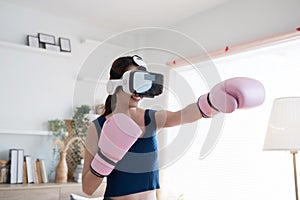 Young Asian woman fighter boxer fit girl in VR glasses wearing boxing gloves playing a boxing game at home.