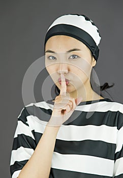 Young Asian woman with finger on lips in prisoners uniform