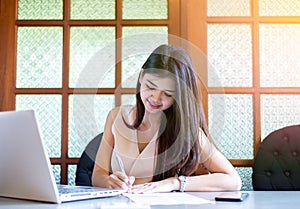 Young asian woman Freelancer smile and using labtop and writing note in college library