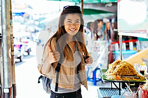 Young Asian woman giving a thumbs up gesture in front of street food stall