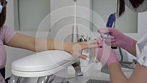 Young Asian woman with glasses in a manicure salon. A manicurist uses a drill machine to remove nails.