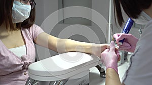 Young Asian woman with glasses in a manicure salon. A manicurist uses a drill machine to remove nails. The camera zooms
