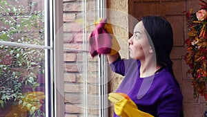 Young Asian Woman in gloves cleaning window with rag and cleanser spray at home