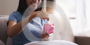 Young asian woman hand putting coins in pink piggy bank for account save money. saving money, retirement fund