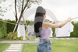 Young asian woman hanging laundry on washing line for drying against blue sky outdoor