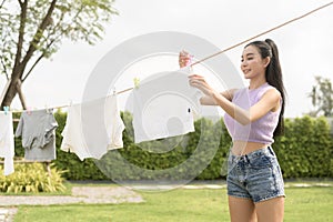 Young asian woman hanging laundry on washing line for drying against blue sky outdoor