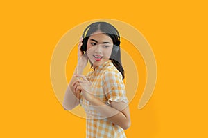 Young Asian woman happy listen to music with headphone on yellow background