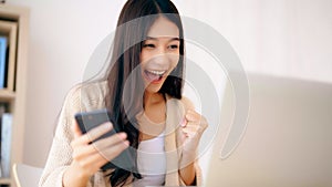 Young asian woman happy working on computer laptop and hand typing chat message on mobile smartphone at home