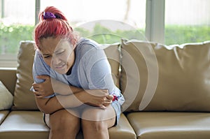 Young Asian woman has menstrual cramps or stomach pain from other causes. She sits on the sofa