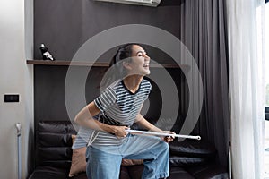 young asian woman having fun during cleaning, fooling with mop and broom