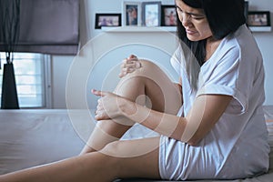 Young asian woman having a knee pain,Female feeling exhausted and painful on bedroom