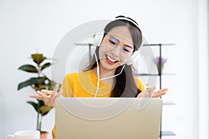 Young asian woman in headphone having conversation chatting while using laptop at house