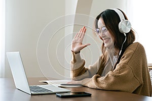 Young asian woman in headphone having conversation chatting while using laptop at house