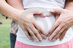 Young asian woman and her husband together caressing her pregnant belly holding their hands in a heart shape on her baby bump. Pr