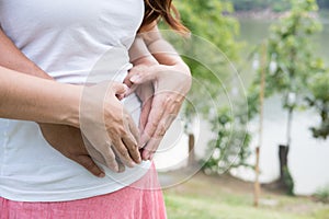 Young asian woman and her husband together caressing her pregnant belly holding their hands in a heart shape on her baby bump. Pr