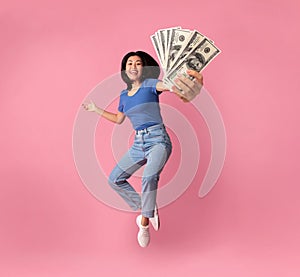 Young asian woman holding bunch of money while jumping