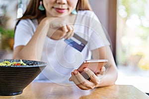 Young asian woman holding a credit card and using smart phone for make an online shopping payment