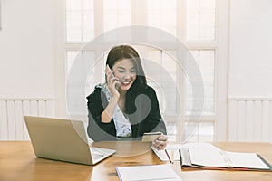 Young asian woman holding credit card and using smart phone for purchase product on internet in home office. Online shopping