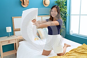 Young asian woman holding pillow sitting on bed at bedroom