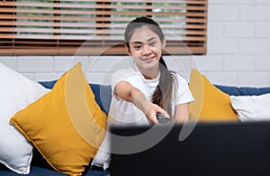 Young asian woman holding remote control and enjoy watching tv in living room at home,sitting on sofa