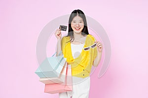 Young asian woman holding shopping bags and showing credit card isolated on color background