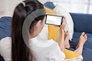 Young asian woman holding smartphone with blank white screen ,lying down cozy on sofa in living room,technology electronic gadget