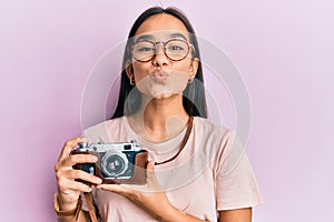 Young asian woman holding vintage camera looking at the camera blowing a kiss being lovely and sexy