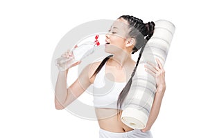 Young asian woman holding yoga mat and drinking water from bottle