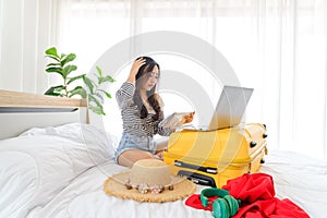 Young Asian woman holds paper map and searching information on computer and planning vacation trip in her bedroom