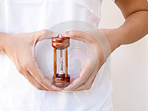 Young asian woman with hourglass in hand at belly, concept time of menstruation cramps and stomach ache, or