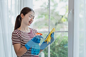 Young Asian woman housewife wearing gloves cleaning glass with microfiber cloth and spray disinfectant
