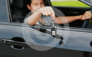 Young asian woman inside a car, hold the key out from the window. Focus at a key hanging at her hand