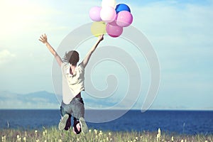 Young asian woman jumping on sunset grassland with colored balloons