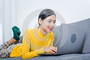 Young asian woman with laptop lying on sofa, work from home WFH concept affected by Coronavirus Covid-19 outbreak