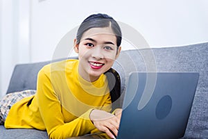 Young asian woman with laptop lying on sofa, work from home WFH concept affected by Coronavirus Covid-19 outbreak