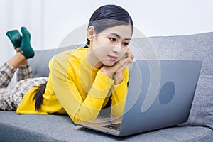 Young asian woman with laptop lying on sofa, work from home WFH concept affected by Coronavirus Covid-19 outbreak