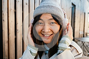Young asian woman laughing and using headphones in cafe outdoors