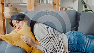 Young asian woman lay down on comfortable sofa in living room sleep after hard time work day and feel sick and bad, tired female