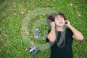 Young Asian woman laying on the green grass listening to music in the park with a chill emotion.