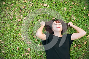 Young Asian woman laying on the green grass listening to music in the park with a chill emotion.
