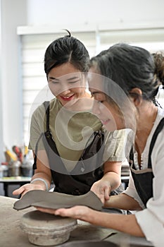 Young asian woman learning to make a clay pottery from professional aged woman potter