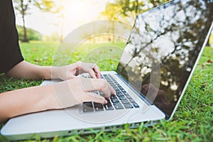 Young asian woman legs on the green grass with open laptop. Girl hands on keyboard. Distance learning concept.