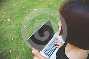 Young asian woman legs on the green grass with open laptop. Girl hands on keyboard. Distance learning concept.