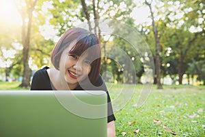 Young asian woman legs on the green grass with open laptop. Girl hands on keyboard. Distance learning concept.