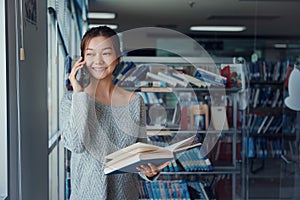 Young Asian woman in the library uses the phone to talk to friends in the library