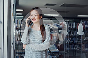 Young Asian woman in the library uses the phone to talk to friends in the library