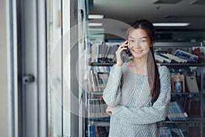 Young Asian woman in the library uses the phone to talk to friends in the library