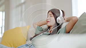 Young asian woman listening to music on couch in living room at home